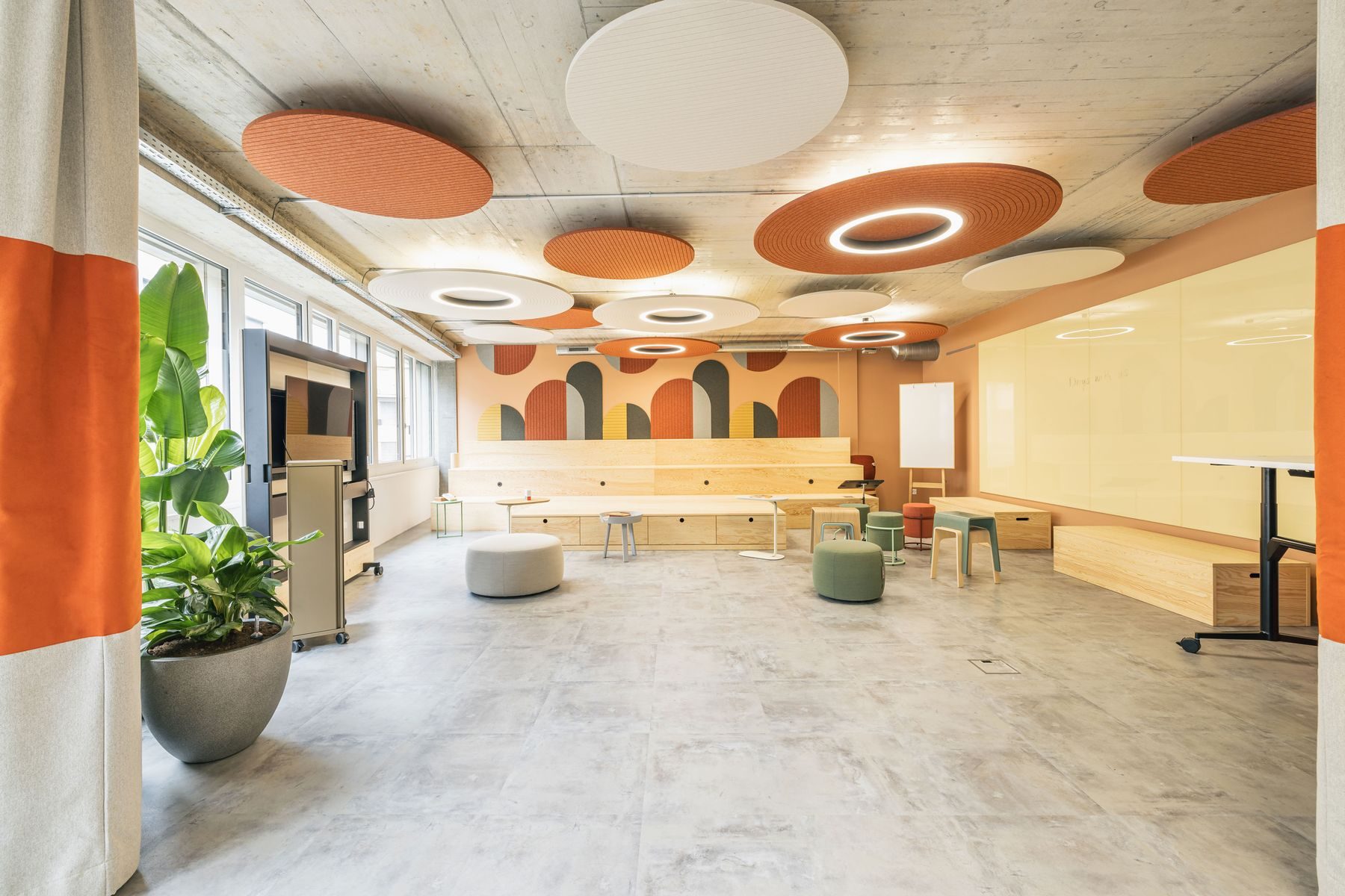 Heller Schulungsraum der Work Factory mit langem Holztisch, runden Akustikelementen an der Decke und Pflanzen