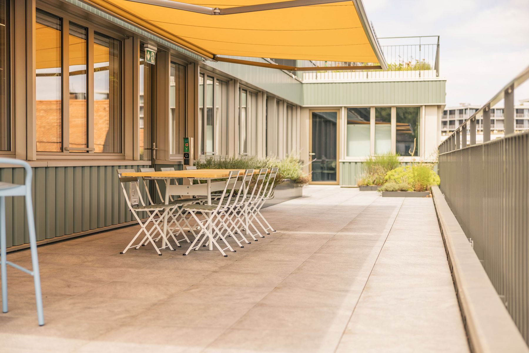 Überdachte Terrasse der Work Factory mit Bistrotischen und Stühlen