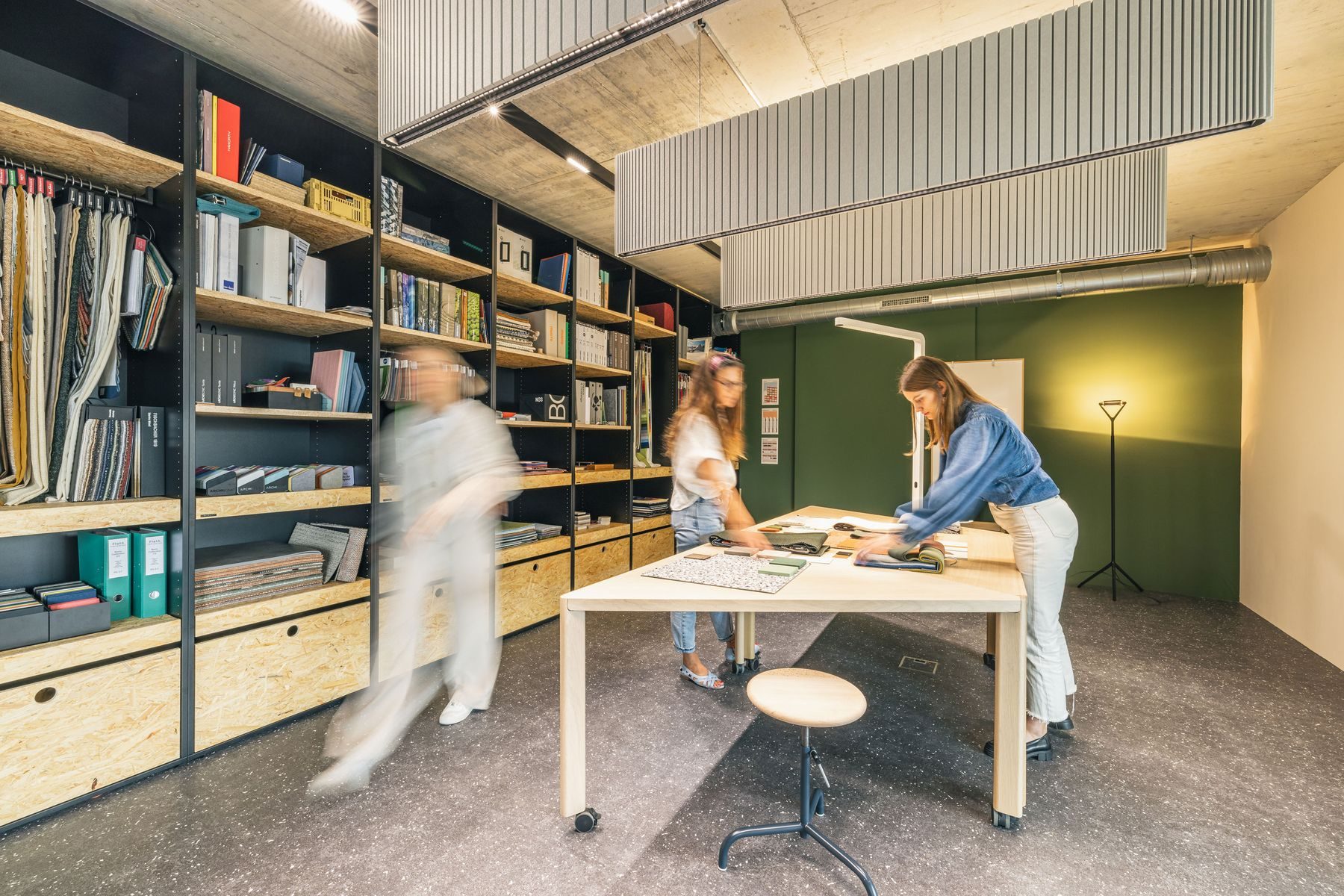 Materialraum der Work Factory mit Regalwand, zwei Personen an einem Arbeitstisch
